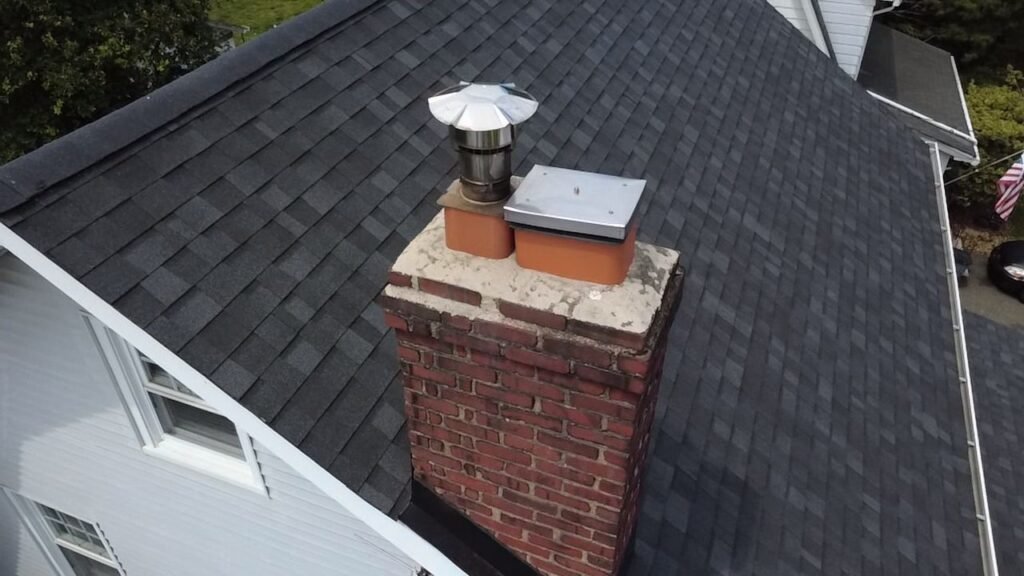 Chimney top showing the crown and existing cap hardware from a rooftop angle
