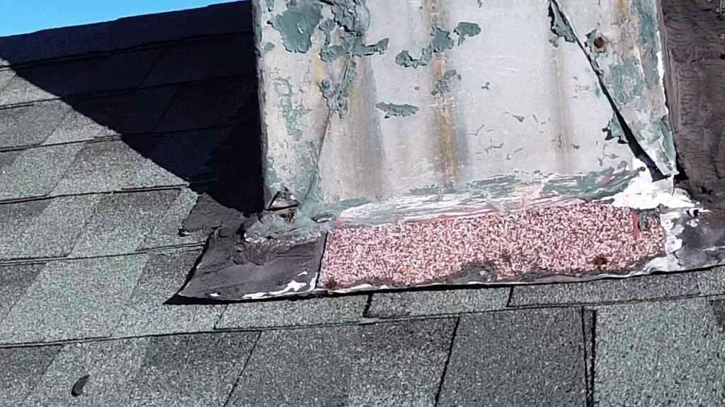 Peeling, deteriorated metal flashing at a roof-chimney junction